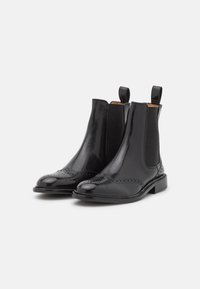 Bottines en cuir noir avec des panneaux élastiques, bout pointu, détails de brogue à l'avant et tirettes pour un enfilage facile.