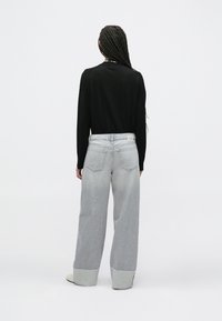 Vide benhvite jeans med oppbrettede kanter, med en bakre midjebåndsmerkelapp og to baklommer; brukt med en svart langermet skjorte.