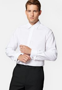 Biała koszula z długim rękawem, z klasycznym kołnierzykiem i zapiętymi mankietami. Posiada subtelną fakturę i kontrastowe spinki do mankietów, w połączeniu z czarnymi spodniami.