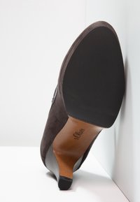 Chaussure à talon haut en suède marron foncé avec bout pointu, semelle noire texturée et nom de la marque s.Oliver sur la semelle intérieure en cuir couleur tabac.