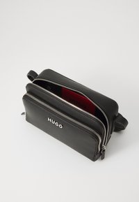 Black leather bag with two zippered compartments. Features silver hardware and a red interior lining with branding. Compact rectangular shape.