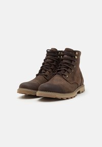 Botas de tobillo de ante marrón con punta redonda, diseño con cordones, ojales de metal y suela de goma con un patrón de banda de rodadura texturizado.