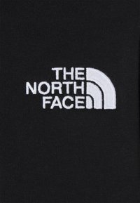 Černá tkanina s vyšívaným bílým logem obsahujícím text "THE NORTH FACE" a půlkruhový motiv. Hladká textura, bez vzorů.