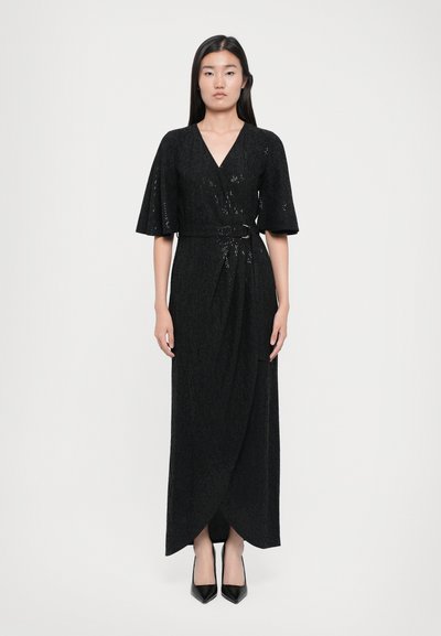 Robe noire enveloppante avec un décolleté en V, des manches courtes évasées et une taille ceinturée. Présente un tissu texturé et tombe jusqu'aux chevilles, assortie à des talons pointus.