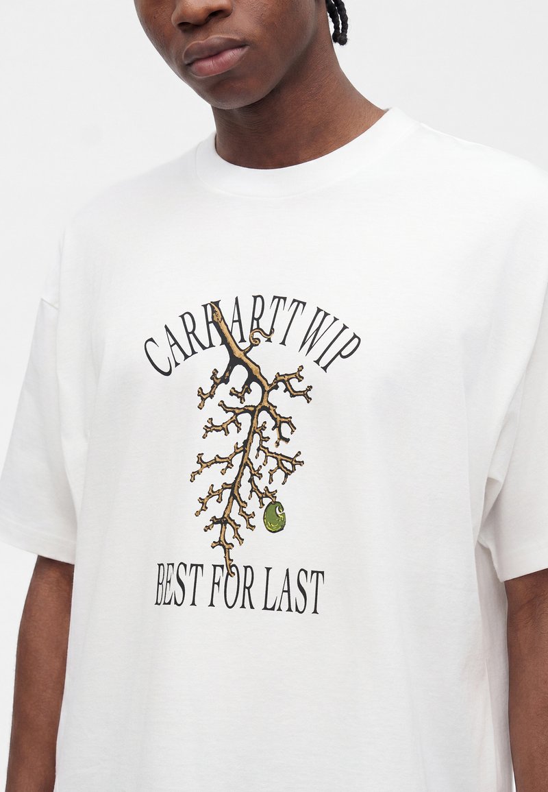 Junge Person trägt ein weißes T-Shirt mit einem Zweigdesign und dem Text "Carhartt WIP Best For Last" auf der Vorderseite.