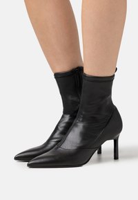 Schwarze Leder-Stiefeletten mit figurbetontem Design, spitzer Zehenpartie und einem 4 cm hohen Stilettoabsatz. Verfügen über einen seitlichen Reißverschluss für leichtes An- und Ausziehen.