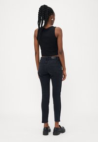 Fekete cropped tank top fekete, magas derekú skinny farmerral párosítva, amely szoros szabású, sima textúrájú és diszkrét hát zsebet tartalmaz.