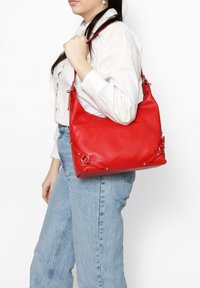 Borsa a tracolla in pelle rossa con finitura testurizzata, dettagli in metallo argentato e manico, mostrata su uno sfondo bianco.