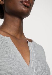 Maglione grigio a maglia con scollo a V. Presenta una texture a coste e un logo bianco "Calvin Klein" lungo la patta.