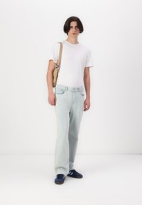 Jeans en denim bleu clair avec une coupe décontractée, associés à un t-shirt blanc uni et des baskets bleues. Un sac à bandoulière beige est porté en travers du corps.
