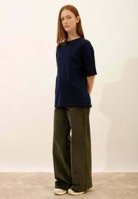 Granatowa, krótko rękawowa dzianinowa bluzka w połączeniu z szerokimi oliwkowymi spodniami. Obuwie w neutralnym kolorze. Gładka textura, luźna sylwetka.