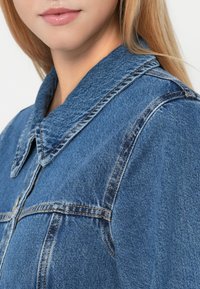 Gaiši zila džinsa jaka ar klasiskām apkaklēm, pogu aizdari un kontrastējošiem izšuvumiem gar šuvēm. Mīksta teksturēta auduma.