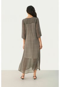 Robe longue et transparente avec un motif en zigzag en noir et crème. Elle présente des manches trois-quarts et une silhouette fluide longueur cheville.