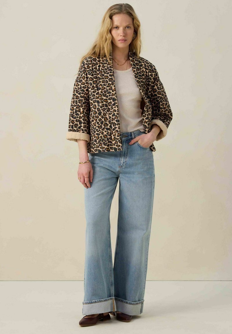 Jas met panterprint en opgerolde mouwen, gecombineerd met lichtblauwe denim jeans met wijde pijpen, voorzien van een rafelige zoom en een ontspannen pasvorm. Bruine schoenen.