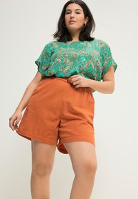 Zelený top s paisley vzorem a krátkým rukávem, doplněný o oranžové lněné šortky. Tento outfit má volný střih a texturovanou tkaninu.