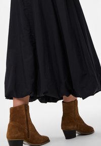 Falda negra fluida con un dobladillo fruncido, combinada con botas de tobillo de ante marrón con cremallera lateral y tacón apilado.