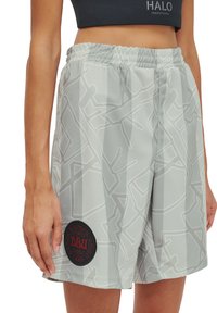 Kvinna som bär gråmönstrade träningstights med en svart och röd cirkulär applikation på vänster ben och en svart kortärmad topp.