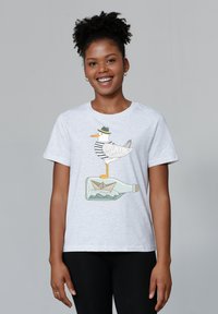 Lichtgrijze katoenen t-shirt met een meeuw in een gestreept shirt die op een fles staat met een papieren bootje erin. Korte mouwen, ronde hals.