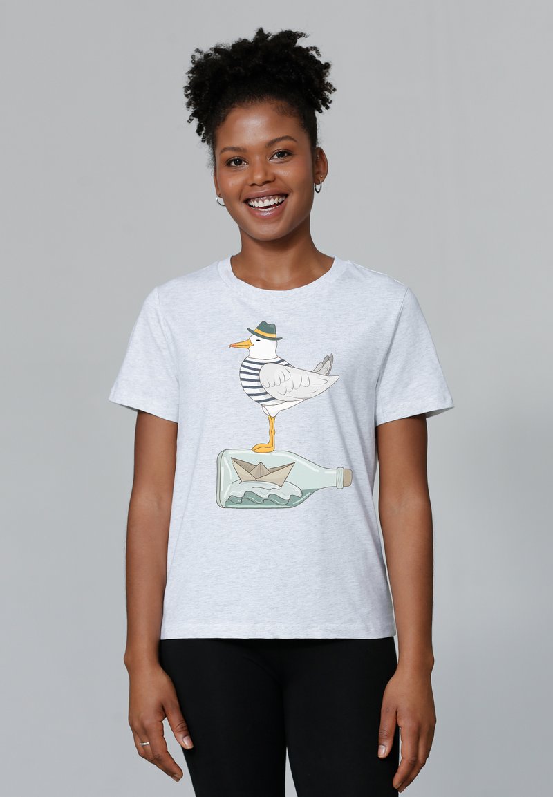 Lichtgrijze katoenen t-shirt met een meeuw in een gestreept shirt die op een fles staat met een papieren bootje erin. Korte mouwen, ronde hals.