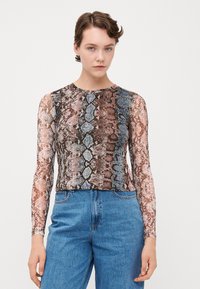 Atasan lengan panjang yang fitted dengan pola kulit ular berwarna-warni dan tekstur transparan. Dipasangkan dengan celana jins denim biru berpinggang tinggi.