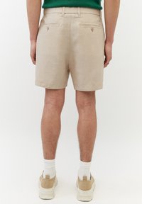 Pantaloni corti beige con un design pulito, realizzati in un tessuto con una sottile texture. Presentano due tasche posteriori con bottoni e orli arrotolati.
