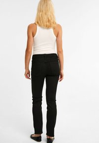 Svarta denimjeans med slim fit, hög midja och bakfickor, som bärs med en vit ribbad tanktop. Slät textur och minimalistisk design.