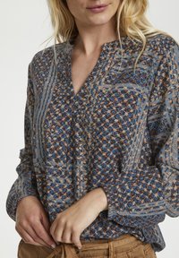 Kwiatowa bluzka z dekoltem w serek, długimi rękawami oraz połączeniem niebieskich, brązowych i beżowych wzorów na lekkim materiale. Teksturowany detal.