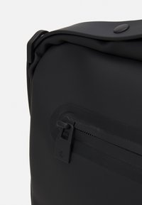 Schwarze wasserdichte Tasche mit glatter Textur, ausgestattet mit einem Reißverschlussfach und einem Druckknopfverschluss oben. Das Design beinhaltet abgerundete Kanten.