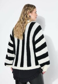 Maglione lavorato a maglia spessa con righe bianche e nere, caratterizzato da una vestibilità ampia, maniche larghe e una texture morbida con un orlo arricciato sotto.