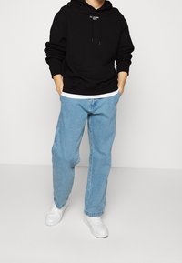 Černá mikina s kapucí a stahovacími šňůrkami, doplněná světle modrými džíny. Bílá sportovní obuv dotváří celý outfit. Jednoduchý design, volný střih.