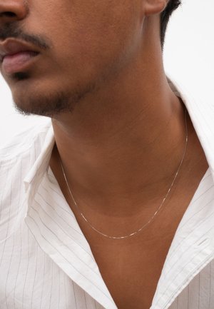 Silver chain necklace worn on a bare neck, contrasting with the skin tone, paired with a white striped collared shirt.