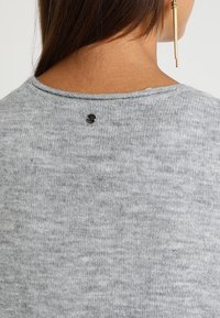 Szary sweter dzianinowy, z okrągłym dekoltem, teksturowym materiałem i małym czarnym guzikiem z tyłu. Zbliżenie z tyłu.