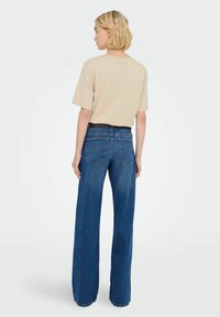 Beige T-shirt met korte mouwen en losse blauwe jeans, met een brede pijp, middelmatig gewassen en twee achterzakken met stikseldetails.