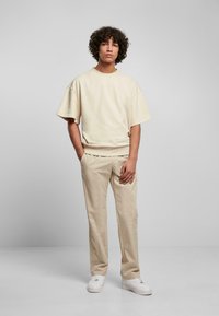 Beige, oversized, rövid ujjú pulóver bézs nadrággal és fehér sportcipővel párosítva. Sima szövet és laza fazon.