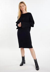 Abito in maglia nera con maniche lunghe e ampie e una vestibilità comoda. Abbinato a stivaletti neri alla caviglia. Texture liscia e design a lunghezza media.