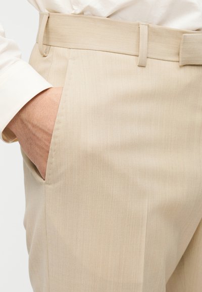 Μπεζ παντελόνια σε ίσια γραμμή με απαλό, υφασμάτινο ύφασμα με υφή. Διαθέτουν επίπεδη μπροστινή όψη, θηλιές για ζώνη και πλαϊνή τσέπη. Καθαρός, μοντέρνος σχεδιασμός.