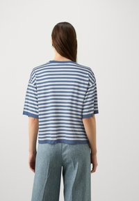 Pasiasty krótki rękaw w kolorze niebieskim i szarym, charakteryzujący się luźnym krojem, okrągłym dekoltem oraz teksturowanym splotem. Noszony z jasnoniebieskimi spodniami typu wide-leg.