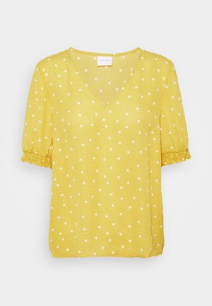 Blouse jaune à manches courtes avec pois blancs, col en V et poignets élastiqués aux manches.