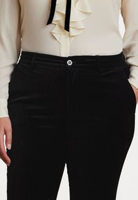Pantaloni din catifea neagră cu față plată, curea, și buzunare frontale. Închidere cu buton la talie. Textură moale și croială ajustată.
