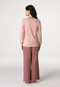 Blusa a maniche lunghe color blush con scollatura arrotondata abbinata a pantaloni larghi rosa. Entrambi i capi hanno una texture liscia e morbida.