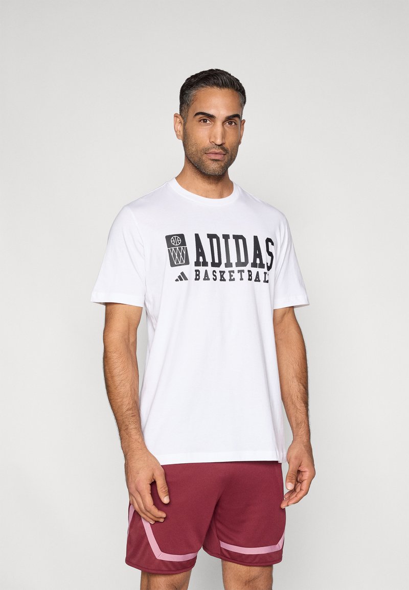 Λευκό μπλουζάκι με μαύρο γράφημα "ADIDAS BASKETBALL", συνδυασμένο με μπορντό σορτς με ροζ λεπτομέρειες και πλαϊνές τσέπες.