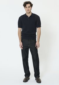 Polo à manches courtes bleu marine avec motif en maille texturée, col à revers et deux boutons, associé à un jean en denim foncé et des chaussures marron.