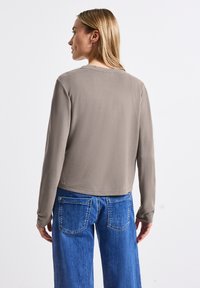 Hnědý top s dlouhým rukávem vyrobený z hladkého materiálu, s kulatým výstřihem a zkráceným designem, doplněný o vysoce pasové modré džíny.