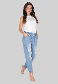 Biała bezrękawnik, jasnoniebieskie dżinsy dresowe z dziurami, elastycznym pasem, bocznymi kieszeniami i mankietami. Beżowe sandały na obcasie.