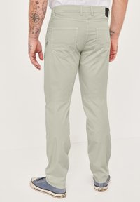 Hellgraue Hosen mit schlanker Passform, ausgestattet mit zwei Gesäßtaschen und einem strukturierten Stoff. Kombiniert mit blauen Sneakers mit weißen Sohlen.