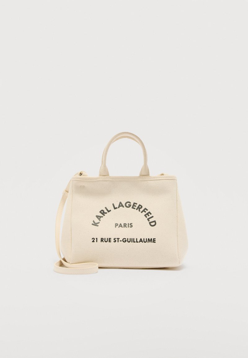 Μπεζ τσάντα tote από καμβά Karl Lagerfeld με λαβές, αποσπώμενο λουρί και μαύρο κείμενο «Karl Lagerfeld Paris 21 Rue St-Guillaume» στο μπροστινό μέρος.