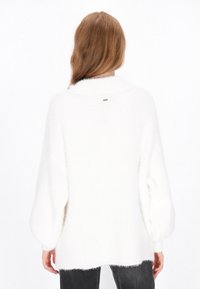 White oversized knit sweater with a soft, fluffy texture, drop shoulder seams, and a subtle logo detail at the back.
