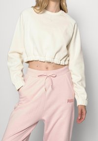 Avskuren krämfärgad sweatshirt med elastisk nederkant och mudd, parat med mjuka rosa sportbyxor med elastisk midja och sidofickor.