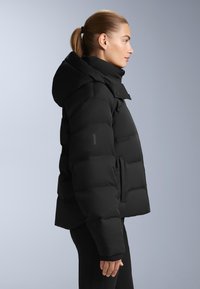 Crna puf jakna s kapuljačom, s karakterističnim kvadratnim šavovima, zatvaranjem na dugmad i elastičnim manžetama. Teksturirani, vodootporni materijal.