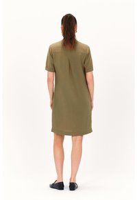 Vestito a camicia verde oliva con maniche corte, dettaglio della piega sul retro e orlo dritto. Indossato con scarpe ballerine nere.